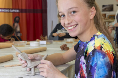une enfant blonde aux yeux bleu, souriant, tenant une figurine qu'elle a sculpté dans ses mains - Agrandir l'image 9 sur 9, fenêtre modale